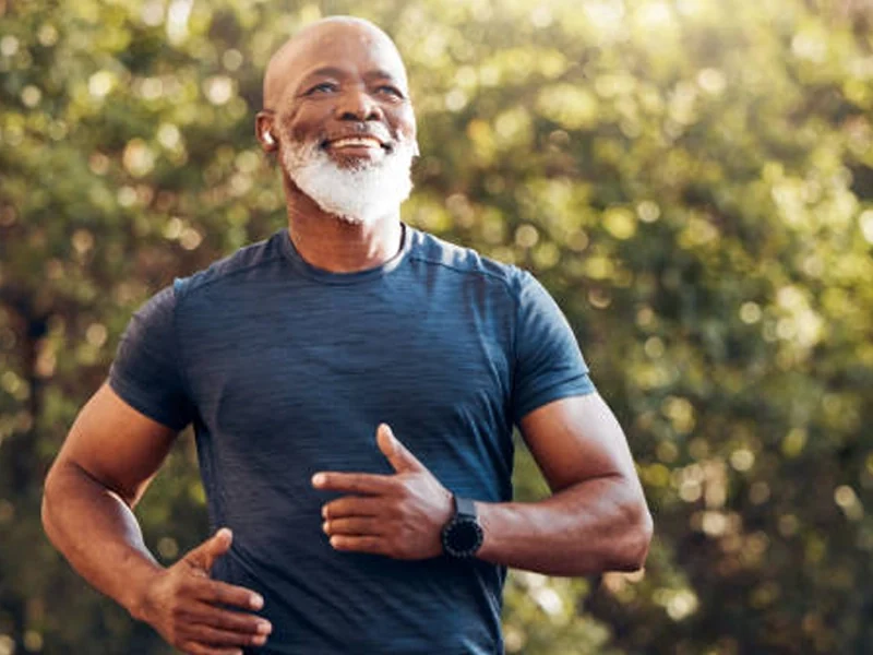 An older man jogging among sunlit trees